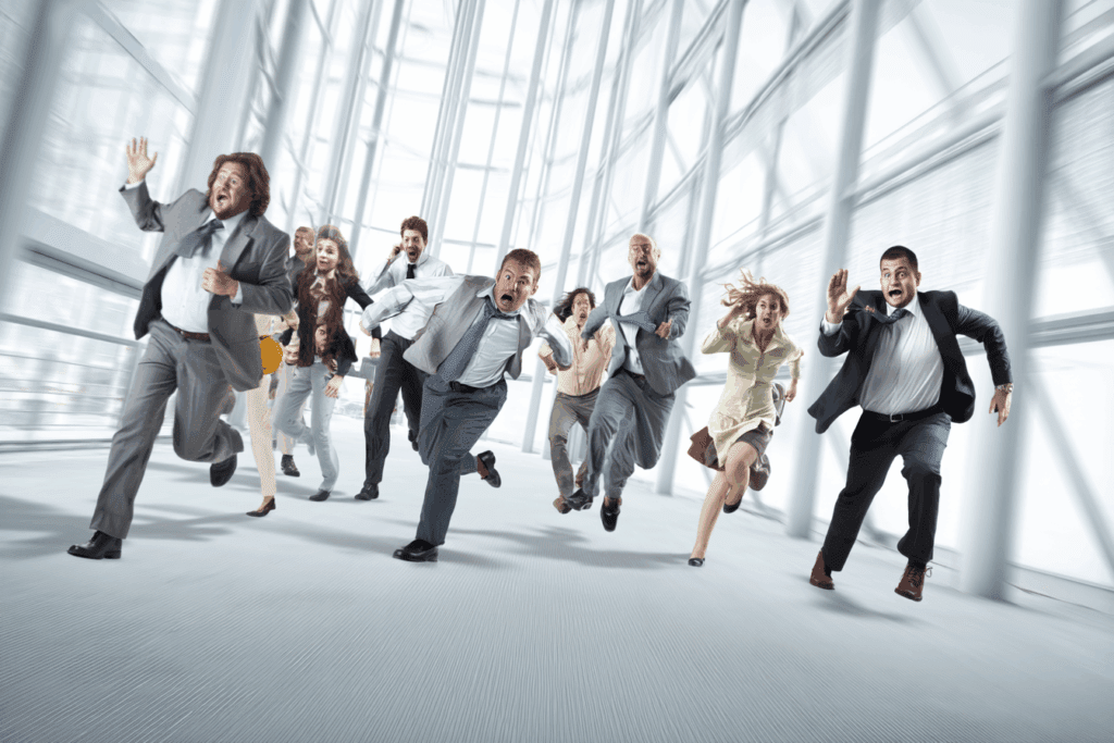 Businesspeople frantically running in circles inside an office, panicking without any real danger present. Represents human overreaction to technology