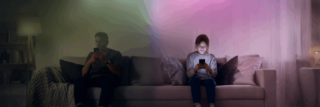 A parent and teenager sit on opposite ends of a couch, each focused on their own phone, with colored lighting dividing the space between them.