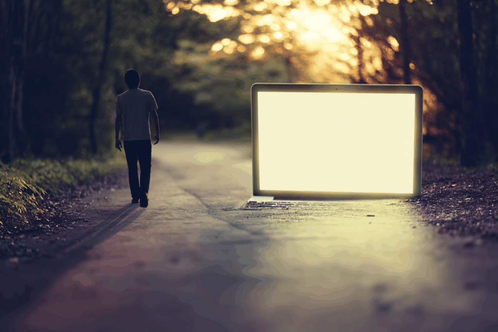 A person walks down a quiet forest road at sunset, leaving behind a glowing laptop screen placed in the middle of the path. The warm light and natural setting evoke a sense of peaceful disconnection from technology and return to the real world.
